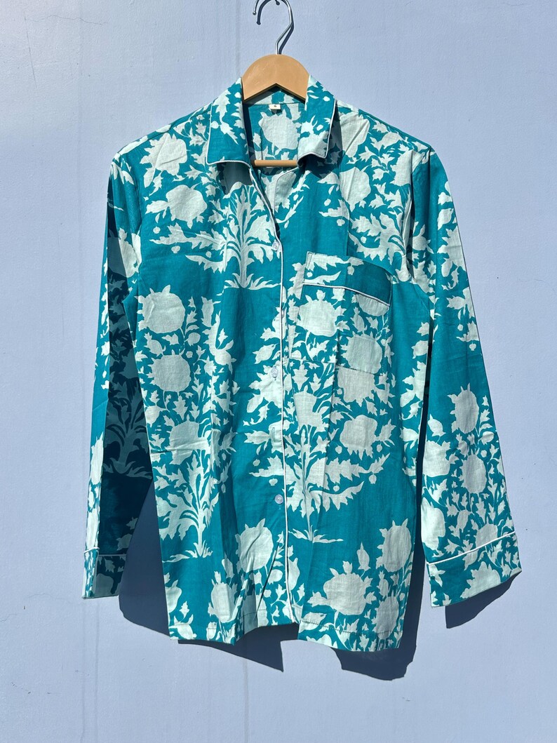 Pu&ograve; includere: Una camicia a maniche lunghe blu turchese con una stampa floreale bianca. La camicia ha una chiusura con bottoni sul davanti e una tasca sul petto sinistro.
