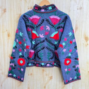 K&ouml;nnte beinhalten: Eine blaue bestickte Jacke mit hohem Kragen und langen &Auml;rmeln. Die Jacke hat ein Blumenmuster in Rot-, Rosa-, Gr&uuml;n- und Schwarzt&ouml;nen.