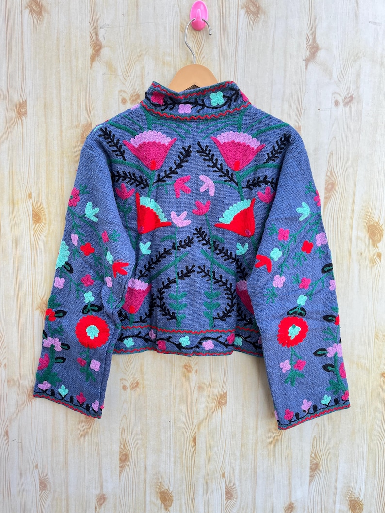 K&ouml;nnte beinhalten: Eine blaue bestickte Jacke mit hohem Kragen und langen &Auml;rmeln. Die Jacke hat ein Blumenmuster in Rot-, Rosa-, Gr&uuml;n- und Schwarzt&ouml;nen.