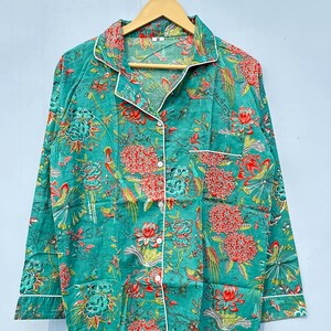 May include: A teal blue long-sleeved shirt with a white trim and a floral print featuring red, orange, and green flowers and birds. The shirt has a button-up front and a collar.