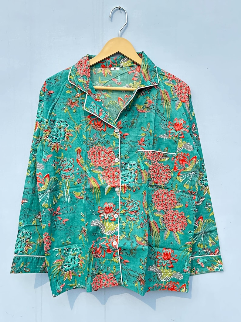 May include: A teal blue long-sleeved shirt with a white trim and a floral print featuring red, orange, and green flowers and birds. The shirt has a button-up front and a collar.