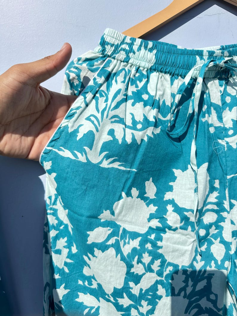 Pu&ograve; includere: Pantaloni da pigiama blu turchese con motivo floreale bianco. I pantaloni hanno un elastico in vita e un cordoncino.