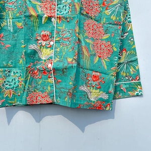 May include: A teal blue button-up shirt with a floral and bird print. The shirt has a white trim around the collar and cuffs.