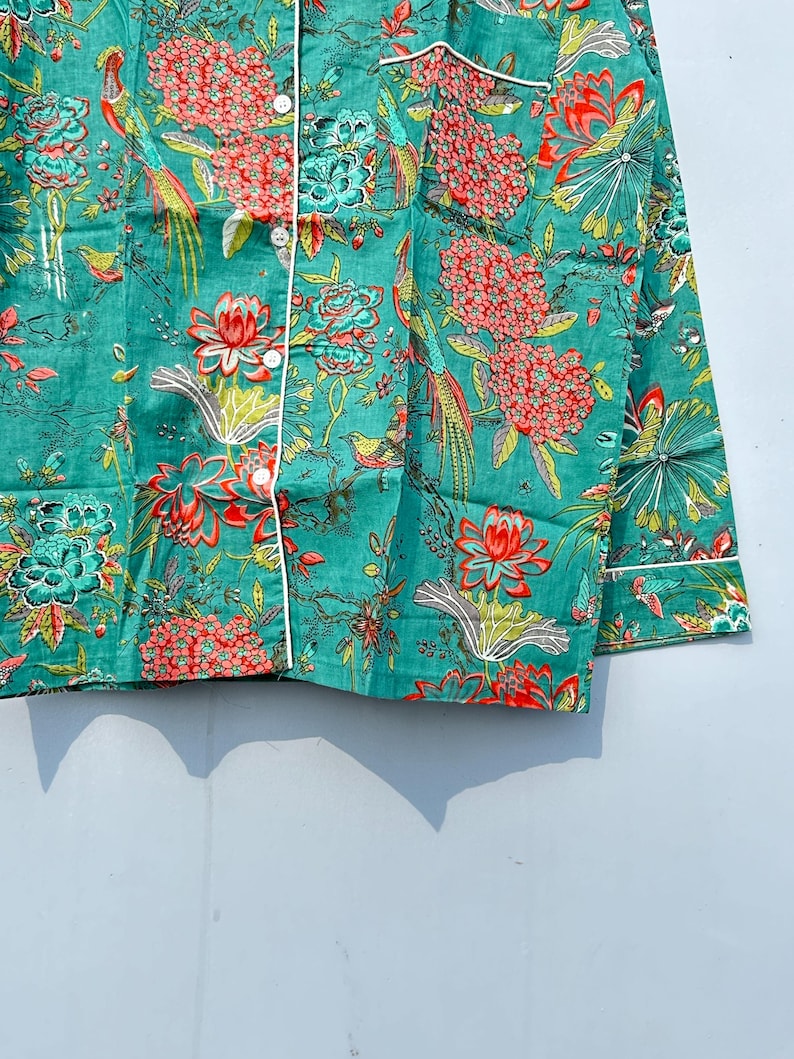 May include: A teal blue button-up shirt with a floral and bird print. The shirt has a white trim around the collar and cuffs.
