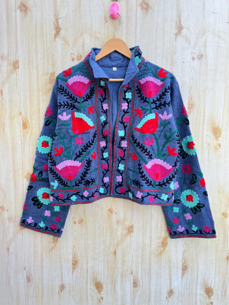 May include: A blue cropped jacket with long sleeves and floral embroidery in shades of pink, red, green, and black.