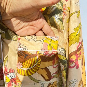Op de afbeelding: Een beige overhemd met knopen en een bloemenprint in tinten geel, bruin, roze en groen. Het overhemd heeft een witte rand rond de kraag en de zak.
