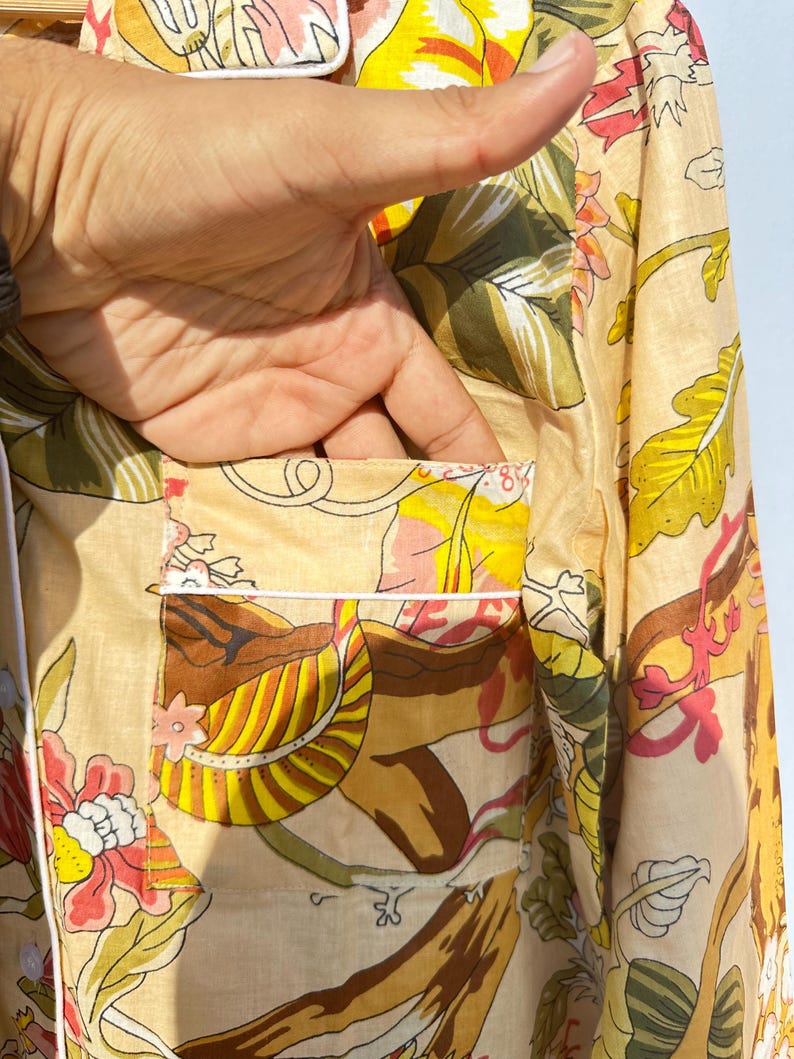 Op de afbeelding: Een beige overhemd met knopen en een bloemenprint in tinten geel, bruin, roze en groen. Het overhemd heeft een witte rand rond de kraag en de zak.