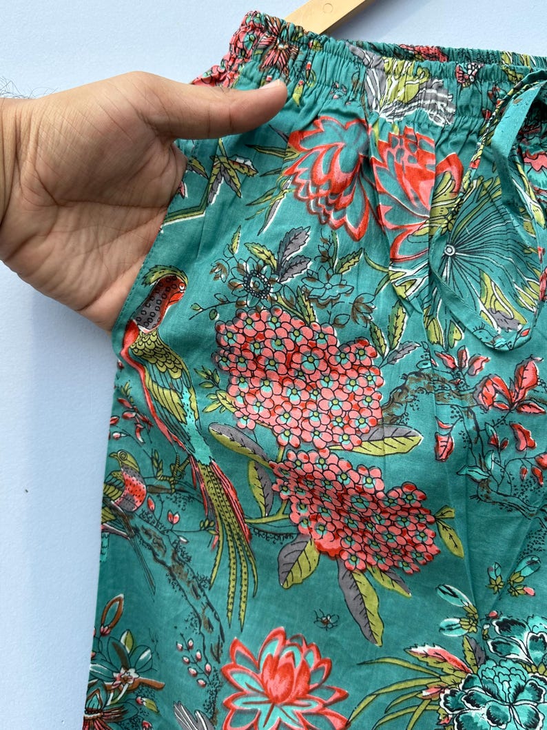 May include: Teal blue cotton fabric with a floral print featuring pink and red flowers, green leaves, and colorful birds. The fabric has a gathered elastic waistband.