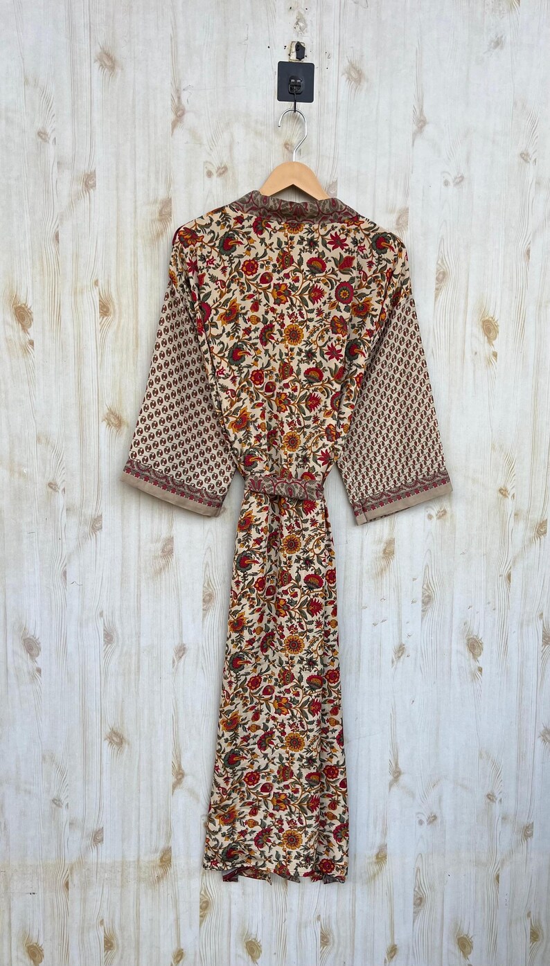 May include: A floral print robe with a cream background, featuring red, orange, and yellow flowers. The sleeves have a repeating geometric pattern in a similar color palette. The robe is hanging on a wooden hanger.