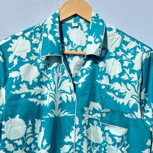 Pu&ograve; includere: Una camicia da pigiama blu turchese con stampa floreale bianca. La camicia ha una chiusura con bottoni sul davanti e una tasca sul lato sinistro.