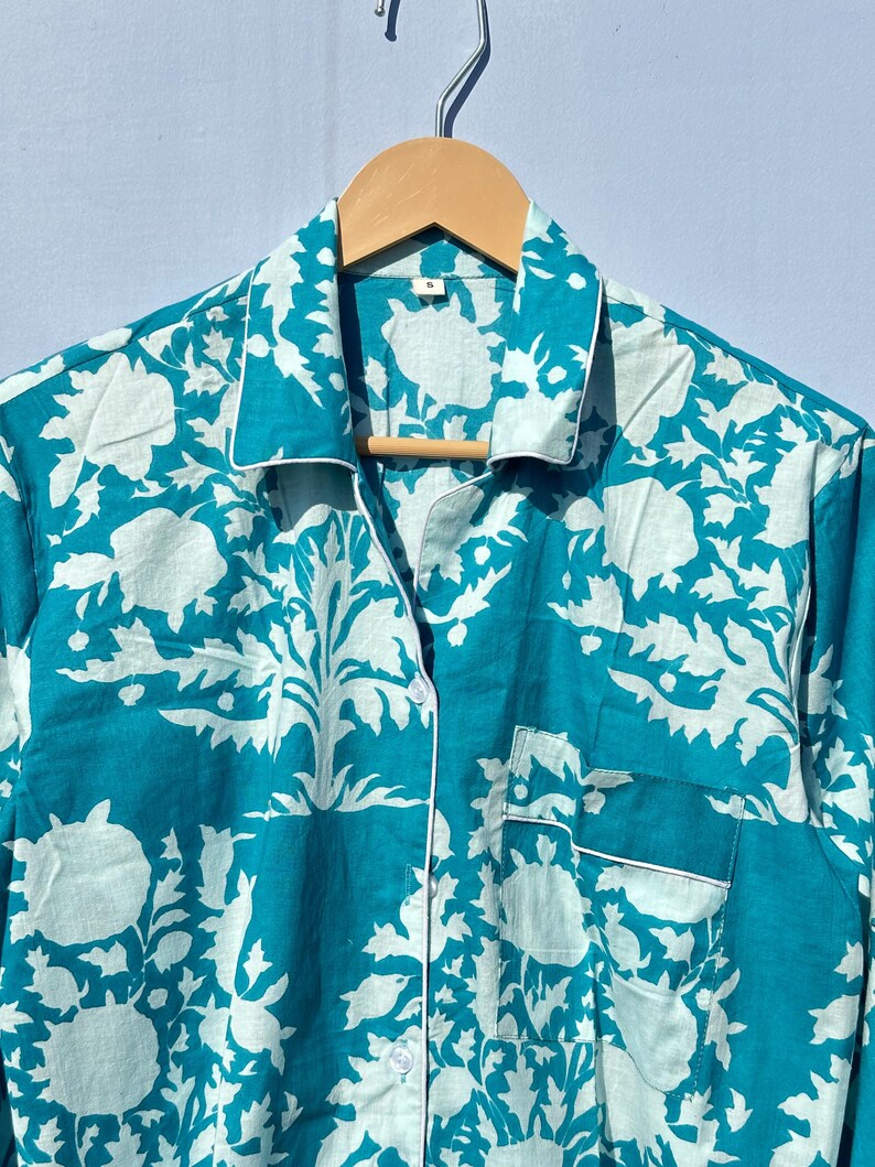 Pu&ograve; includere: Una camicia da pigiama blu turchese con stampa floreale bianca. La camicia ha una chiusura con bottoni sul davanti e una tasca sul lato sinistro.