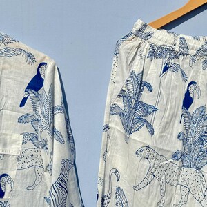 May include: A white pyjama set with a blue tropical print featuring toucans, palm trees and leopards. The set includes a long-sleeved shirt and trousers.
