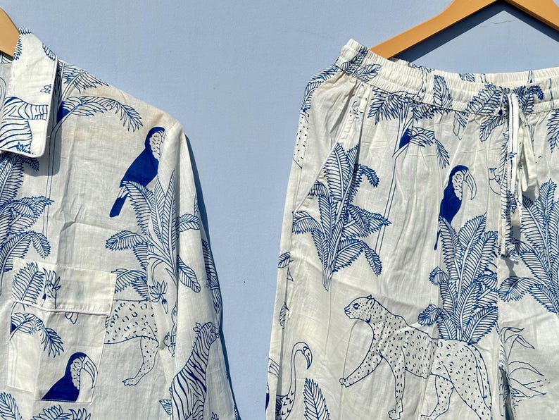 May include: A white pyjama set with a blue tropical print featuring toucans, palm trees and leopards. The set includes a long-sleeved shirt and trousers.