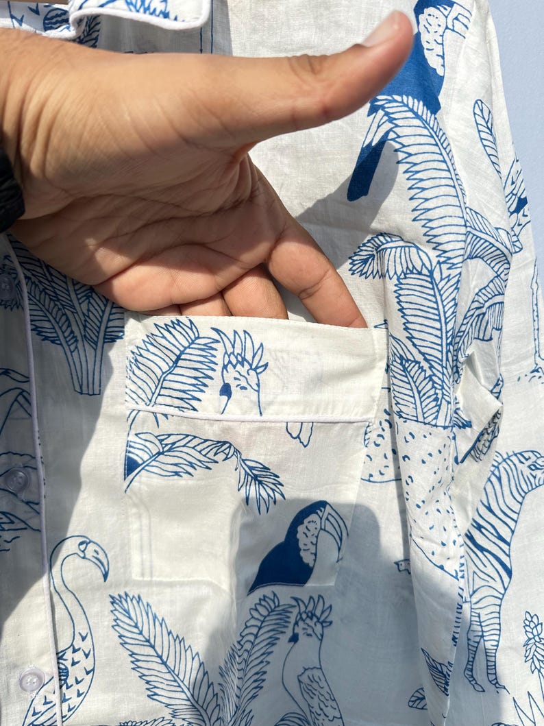 May include: White button-down shirt with a blue and white tropical print featuring toucans, parrots, flamingos, and palm trees. The shirt has a pocket on the left side.
