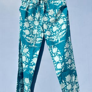 Pu&ograve; includere: Pantaloni blu turchese con stampa floreale bianca. I pantaloni hanno una cintura elastica e un cordoncino.