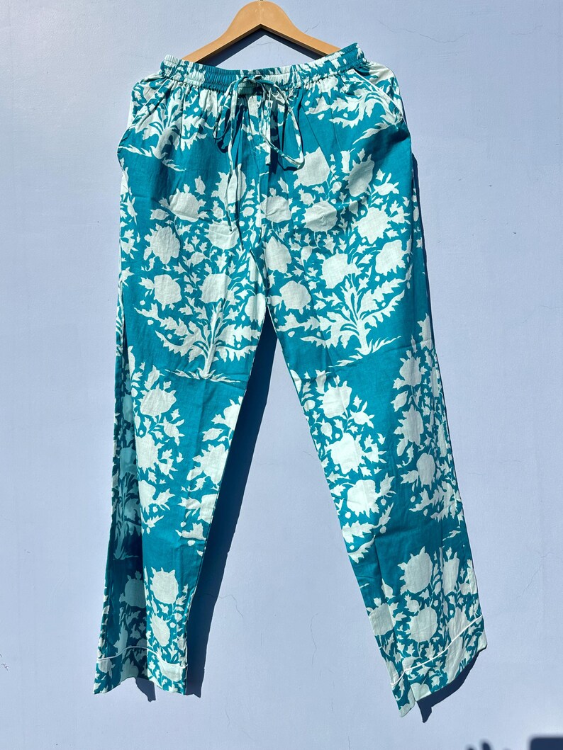 Pu&ograve; includere: Pantaloni blu turchese con stampa floreale bianca. I pantaloni hanno una cintura elastica e un cordoncino.