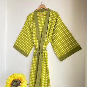 May include: A long, lime green robe with a white checkered pattern and olive green trim. The robe is hanging on a wooden hanger against a white wall. A matching tie belt is wrapped around the waist. The robe is approximately 55 inches long.