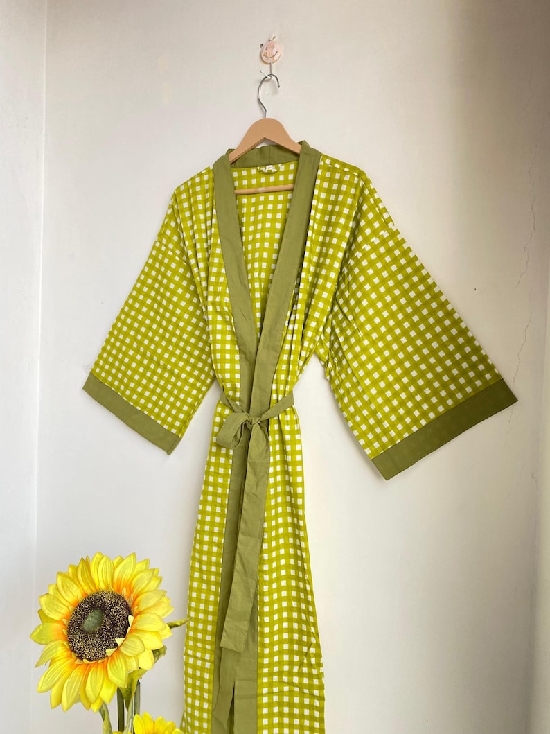 May include: A long, lime green robe with a white checkered pattern and olive green trim. The robe is hanging on a wooden hanger against a white wall. A matching tie belt is wrapped around the waist. The robe is approximately 55 inches long.