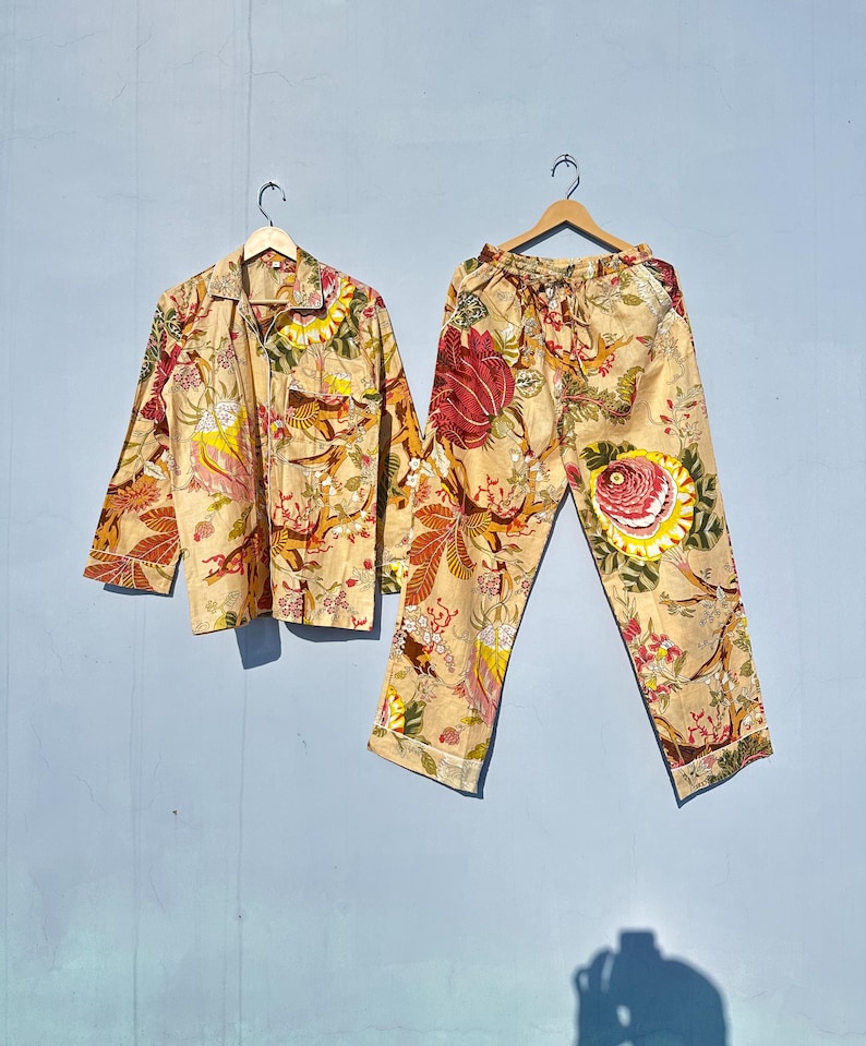 Op de afbeelding: Een beige pyjamaset met een bloemenprint met rode, gele en groene bloemen. De set bevat een shirt met lange mouwen en een broek.