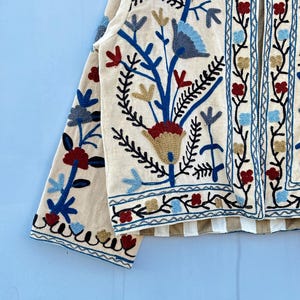Pu&ograve; includere: Una giacca color crema con un ricamo floreale in tonalit&agrave; blu, rosso e oro. La giacca ha una manica lunga e una chiusura anteriore.