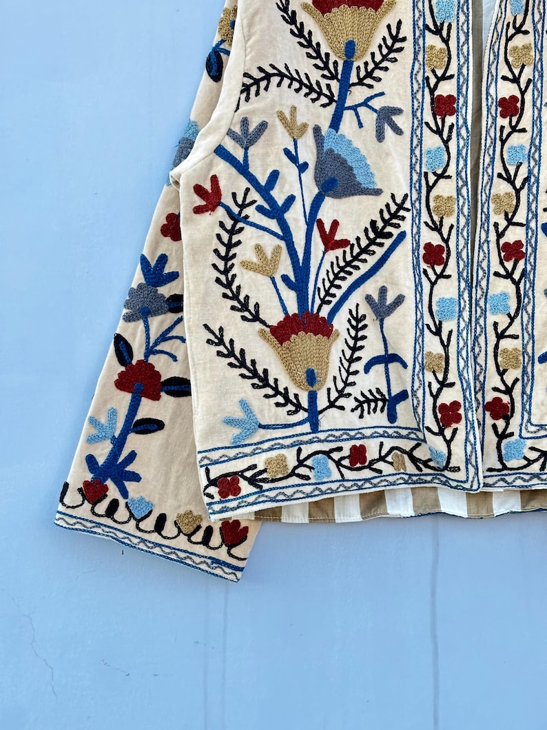Pu&ograve; includere: Una giacca color crema con un ricamo floreale in tonalit&agrave; blu, rosso e oro. La giacca ha una manica lunga e una chiusura anteriore.