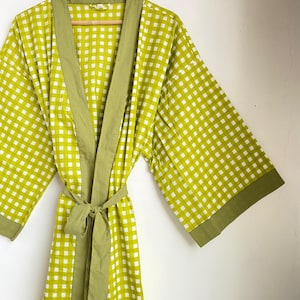May include: A green and white checkered robe with a matching belt. The robe has wide sleeves and a solid green trim along the edges and collar. The robe is hanging on a wooden hanger.