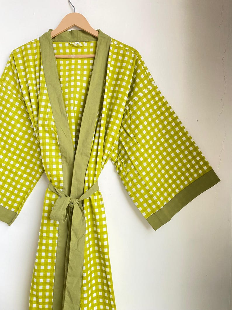 May include: A green and white checkered robe with a matching belt. The robe has wide sleeves and a solid green trim along the edges and collar. The robe is hanging on a wooden hanger.