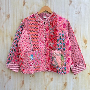 May include: A pink quilted jacket with a patchwork design featuring various floral patterns. The jacket has a mandarin collar, long sleeves, and a zip closure.