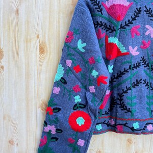 K&ouml;nnte beinhalten: Eine graue, kurze Jacke mit langen &Auml;rmeln und Blumenstickerei in Rot-, Rosa-, Gr&uuml;n- und Blaut&ouml;nen.
