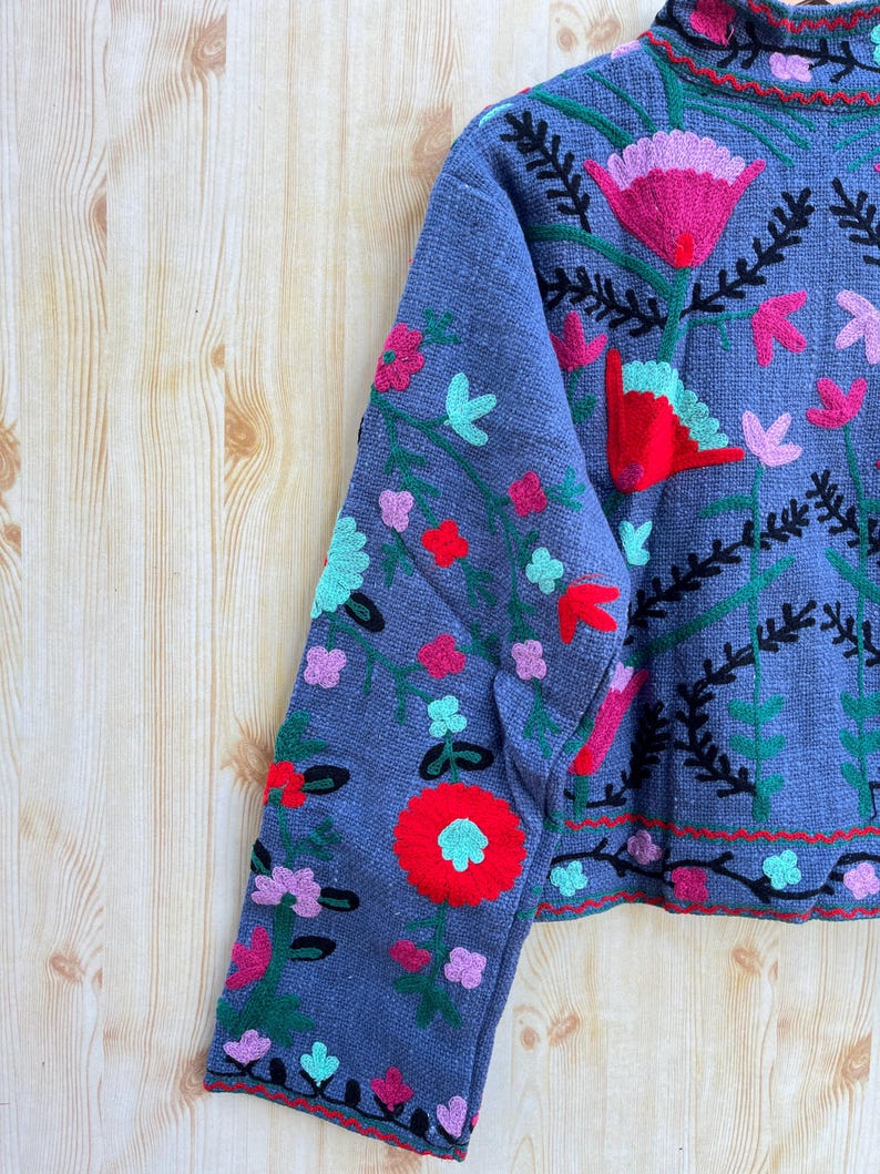 K&ouml;nnte beinhalten: Eine graue, kurze Jacke mit langen &Auml;rmeln und Blumenstickerei in Rot-, Rosa-, Gr&uuml;n- und Blaut&ouml;nen.