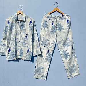 May include: A white pyjama set with a blue and white tropical print featuring toucans and palm trees. The top has a button-up front and long sleeves. The trousers have an elastic waistband.