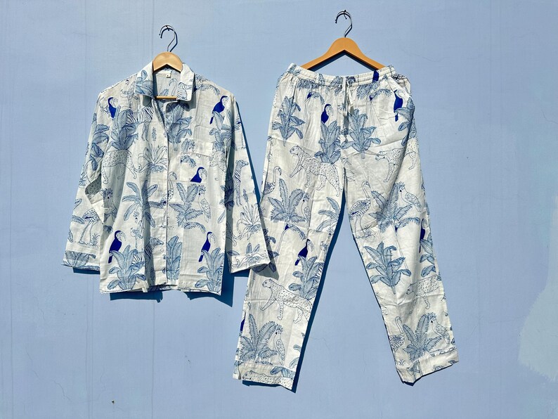May include: A white pyjama set with a blue and white tropical print featuring toucans and palm trees. The top has a button-up front and long sleeves. The trousers have an elastic waistband.