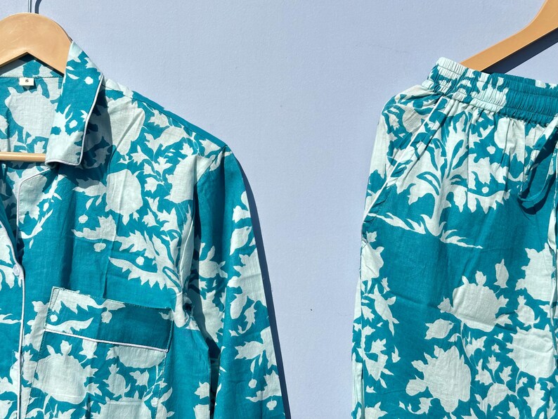 Pu&ograve; includere: Un pigiama blu turchese con un motivo floreale bianco. Il set comprende una camicia a maniche lunghe con bottoni e pantaloni abbinati.