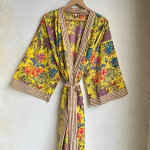 Pu&ograve; includere: Un accappatoio giallo con stampa floreale, finiture a righe e cintura abbinata. L'accappatoio presenta un vivace motivo di fiori e uccelli rossi, blu e rosa. L'accappatoio &egrave; appeso a un'appendiabiti di legno.