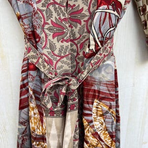 May include: A colorful, patterned robe with a tie belt. The robe features a mix of floral and geometric designs in shades of red, gray, beige, and pink. The tie belt is knotted at the waist.