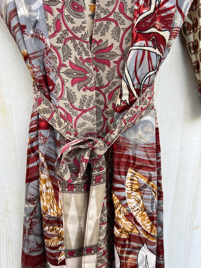May include: A colorful, patterned robe with a tie belt. The robe features a mix of floral and geometric designs in shades of red, gray, beige, and pink. The tie belt is knotted at the waist.