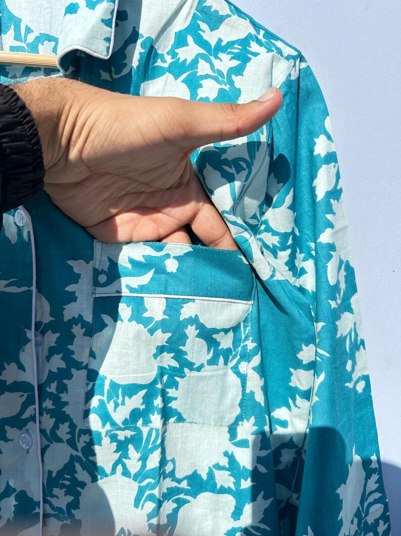 Pu&ograve; includere: Una camicia blu turchese con un motivo floreale bianco. La camicia ha una tasca sul lato sinistro.