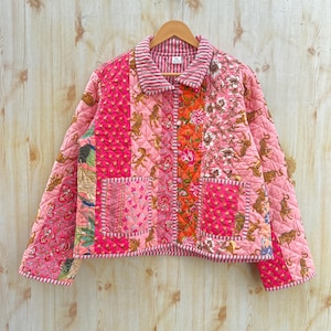 May include: A pink quilted jacket with a patchwork design featuring tigers, flowers, and geometric patterns. The jacket has a button closure and a collar.