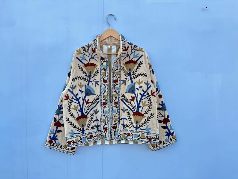 Pu&ograve; includere: Una giacca color crema con un ricamo floreale in tonalit&agrave; di blu, rosso e marrone. La giacca ha una chiusura a zip e maniche lunghe.