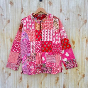 May include: A red and pink patchwork quilted jacket with a button closure. The jacket has a variety of floral and geometric patterns.