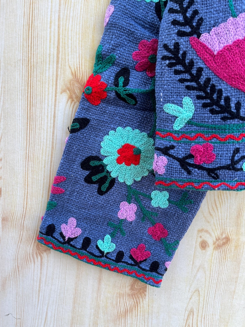 K&ouml;nnte beinhalten: Ein grauer Stoff&auml;rmel mit bunten gestickten Blumen und Bl&auml;ttern. Der &Auml;rmel hat einen roten, gr&uuml;nen und schwarzen Besatz.