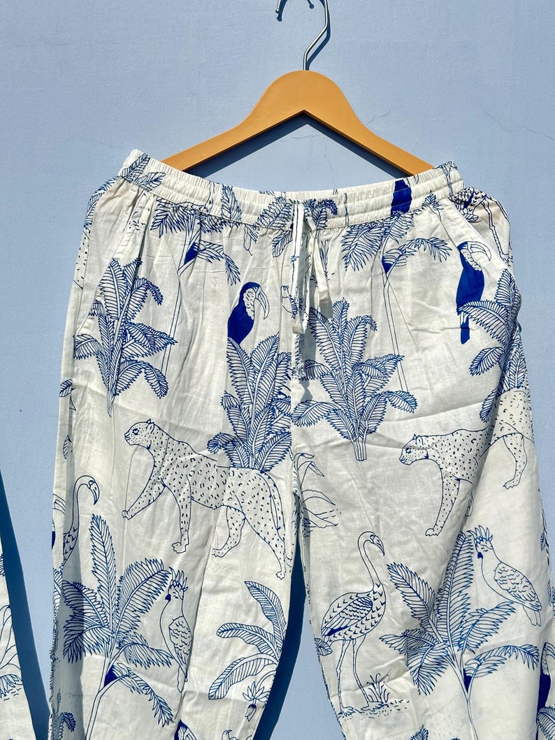 May include: White cotton trousers with a blue tropical print featuring toucans, leopards, and flamingos. The trousers have an elastic waistband and a drawstring.