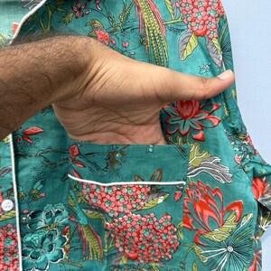 May include: A teal blue pajama top with a white trim and a floral print featuring pink flowers, green leaves, and colorful birds.
