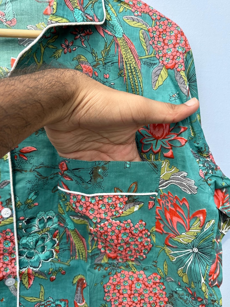 May include: A teal blue pajama top with a white trim and a floral print featuring pink flowers, green leaves, and colorful birds.