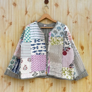 May include: A patchwork quilted jacket with a V-neck and long sleeves. The jacket is made of various fabrics in different colors and patterns, including floral, geometric, and striped designs. The jacket has a green trim around the edges and a button closure.