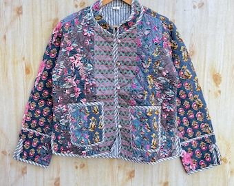 May include: A blue quilted jacket with a floral print. The jacket has a mandarin collar, long sleeves, and a button closure. The fabric is patchwork with different floral patterns.