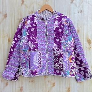 May include: A purple and white quilted jacket with a floral print. The jacket has a button closure and two pockets.