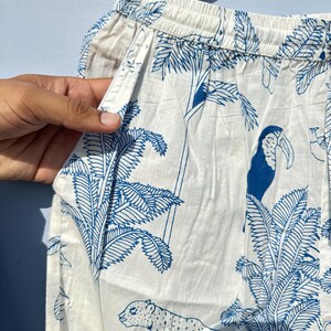 May include: White cotton trousers with a blue and white tropical print featuring a toucan, a leopard, and palm trees.