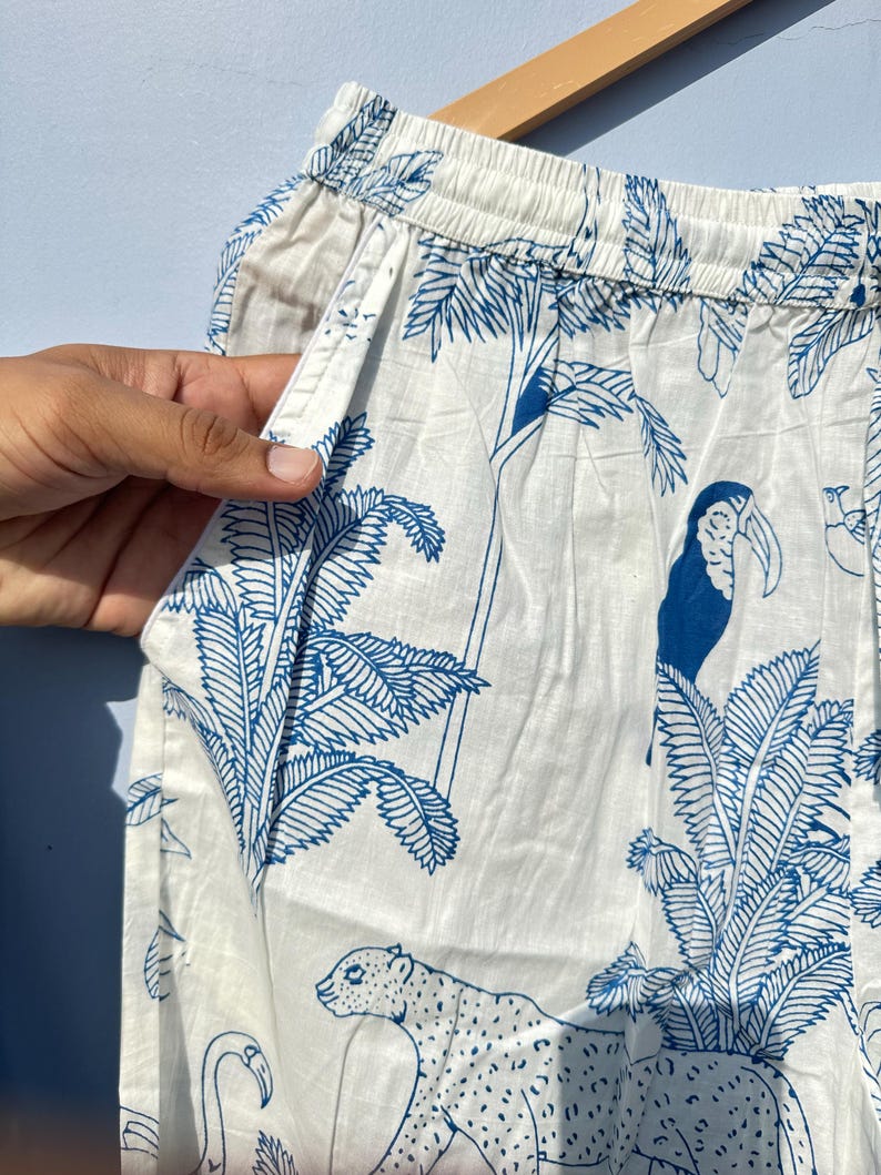 May include: White cotton trousers with a blue and white tropical print featuring a toucan, a leopard, and palm trees.
