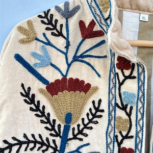 Pu&ograve; includere: Una giacca di velluto color crema con un ricamo floreale in tonalit&agrave; di blu, rosso, verde e marrone. La giacca ha un colletto e una chiusura con bottoni. L'etichetta della taglia sulla giacca riporta "XL".